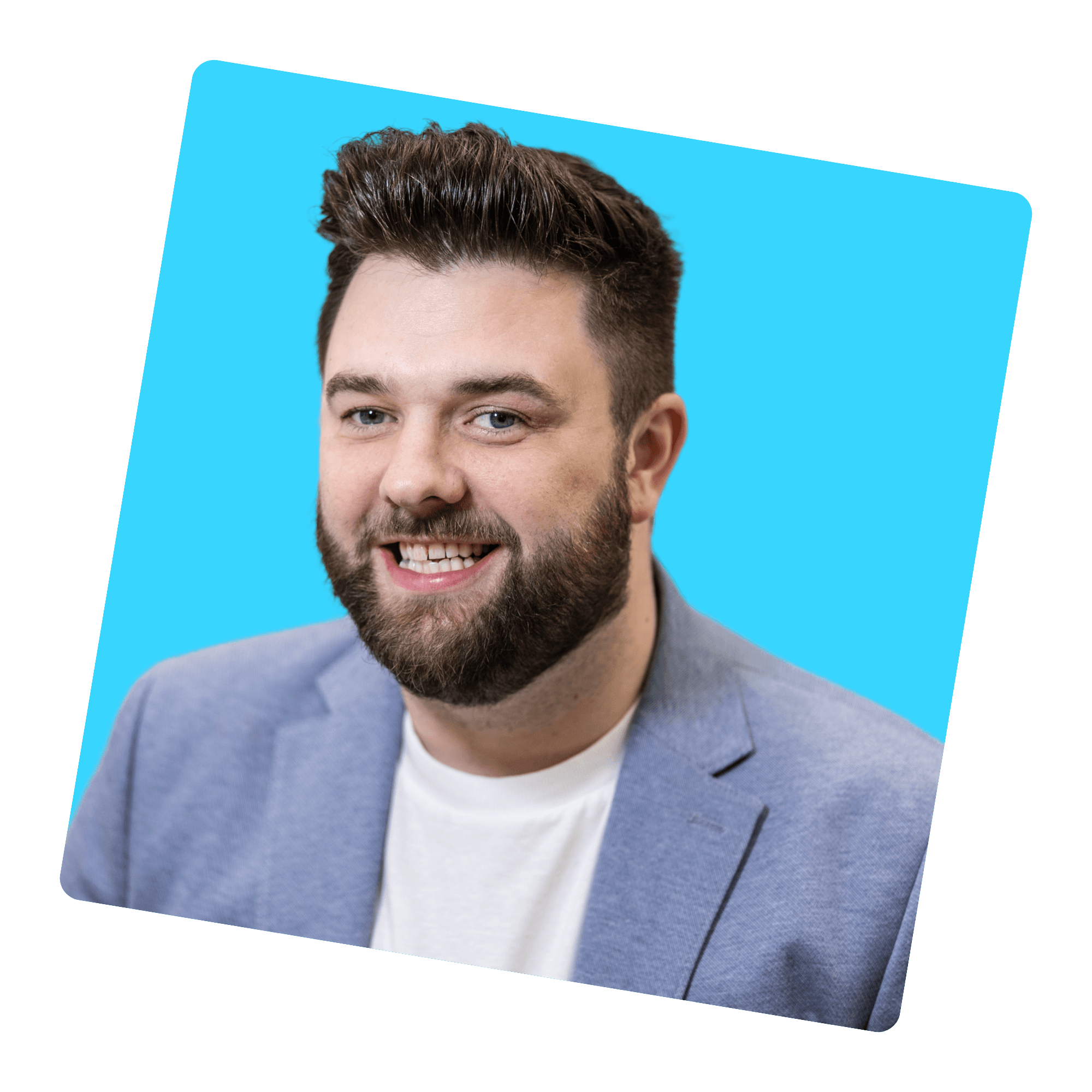 Jamie a white male with dark hair blue eyes and short dark beard smiling at the camera, he is wearing a white t-shirt and blue blazer.