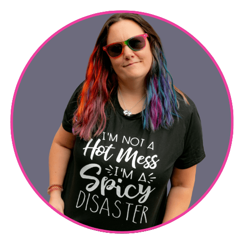 Maddy smiling, with long multicoloured wavy hair, wearing red and green sunglasses and a black T-shirt. 