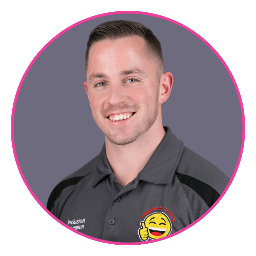 Alex wearing a dark grey collared shirt with embroidered logos, including “Inclusion Champion” and “Happy Smiles Together.