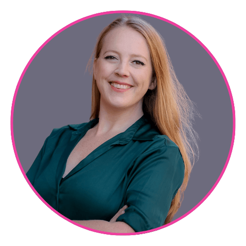 Amy smiling with arms crossed against a grey background, wearing a dark green blouse with a V-neck and collar.