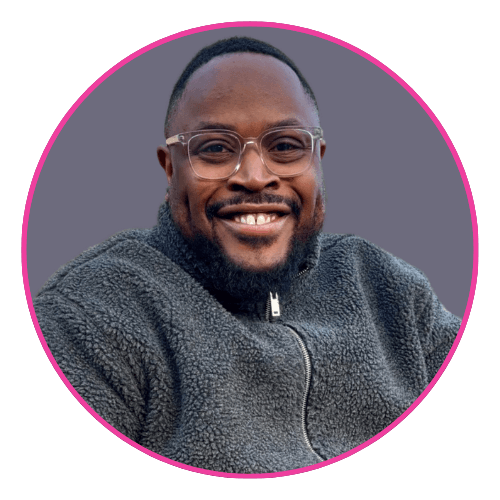 Tumi smiling, wearing clear-framed glasses and a textured dark zip-up jacket.