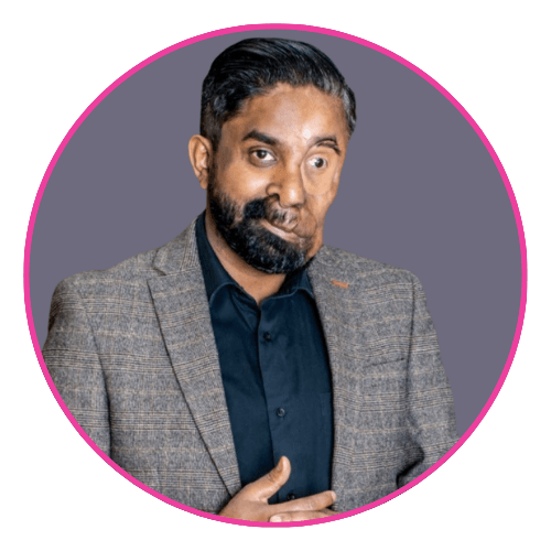 Person standing against a grey background, wearing a brown plaid blazer over a black shirt, with one hand placed on their chest